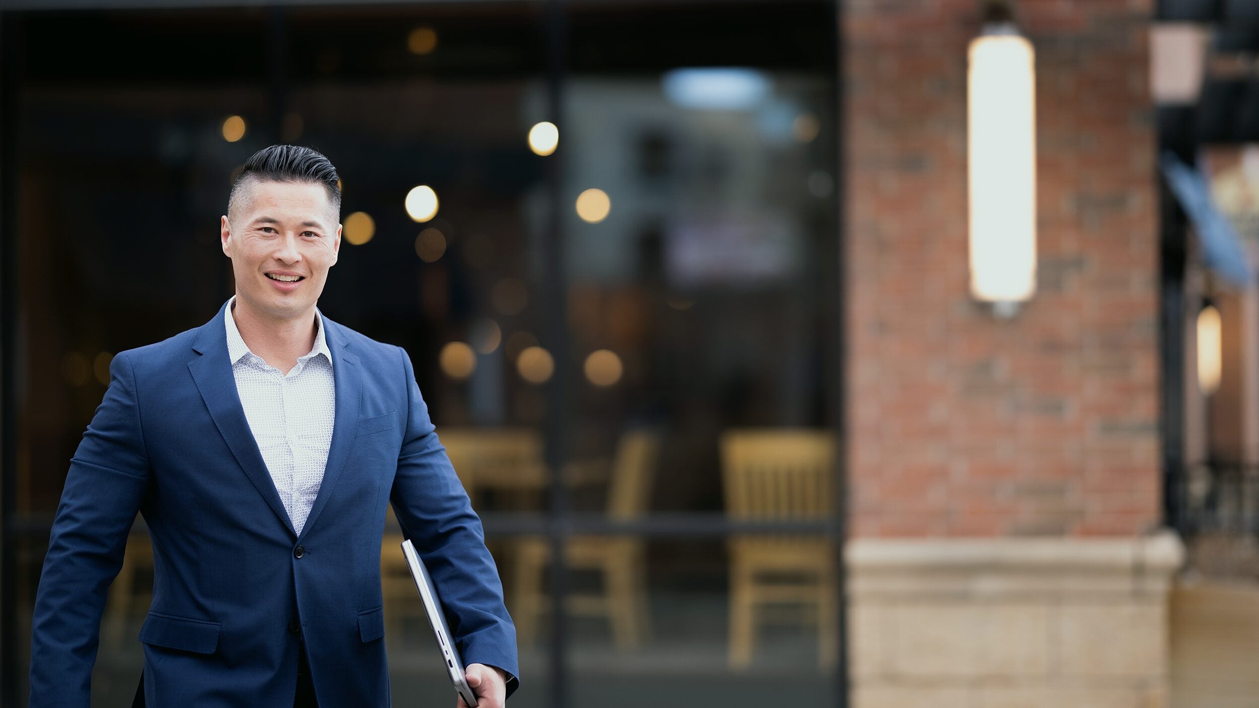 Man carrying laptop walks outside of his workplace.