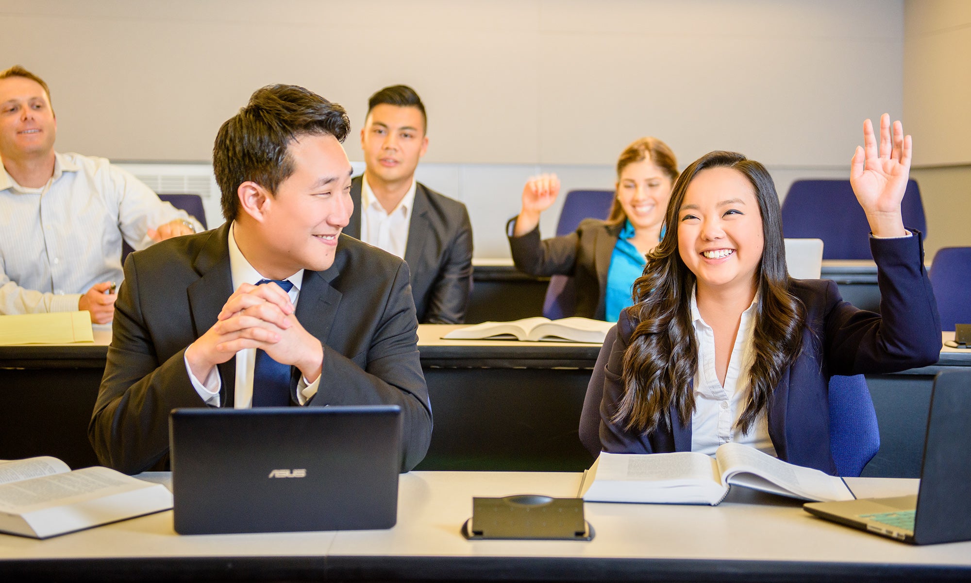 Students sitting in a classroom and a woman raising her hand.